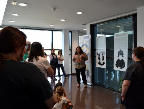 Núria Salán davant dels panells de la Teresa Puig i la Zoe Rosinach amb públic a la visita guiada a l'Enciclopèdia de Dones STEAM a l'IMB-CNM